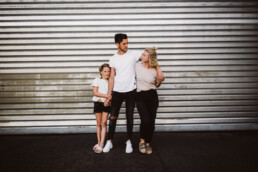 Vater, Mutter und Tochter werden von Nadja Morales vor einem großen Industrietor fotografiert.