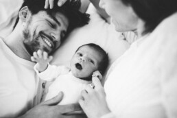 Ein Baby streckt seine Hände aus, während seine Eltern es anlächeln.