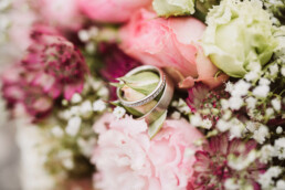 Nadja Morales fotografiert Detailaufnahmen goldener Eheringe an einem Brautstrauß.