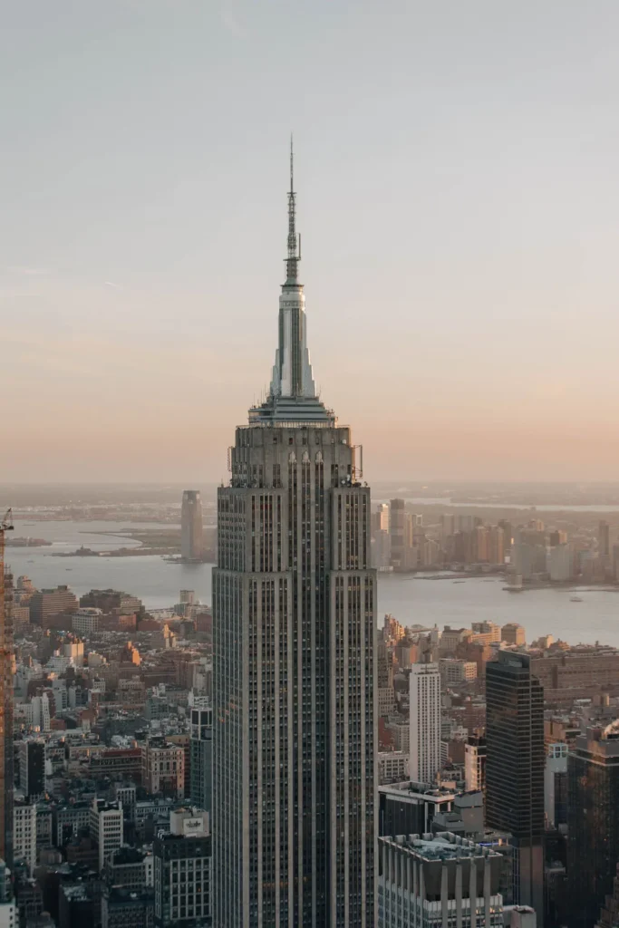 Das Empire State Building erhebt sich vor einem dunstigen Sonnenuntergangshimmel, während im Hintergrund die Stadt und der Fluss zu sehen sind - ein perfekter Ort für ein New Yorker Fotoshooting, aufgenommen von Nadja Morales.